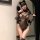 Woman in black lace lingerie set with sheer bodysuit, cat ears, and blindfold posing seductively by mirror.