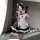 A person wearing a black and white maid costume set, featuring ruffled apron, fishnet stockings, and headband, posing indoors...