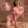 Woman modeling pink nurse costume with open-crotch design, backless skirt, red crosses, and lace-topped stockings.