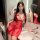 A woman poses in a luxurious bathroom wearing a sheer red sleep dress adorned with pearls and floral patterns, exuding elegan...