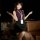 Woman in purple top and black skirt with lanyard, posing beside teddy bear on stool — pure & seductive secretary skirt set.