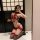 Woman in red sheer chinese-inspired bodysuit with floral embroidery, lace trim, and thigh-high stockings posing indoors.