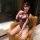 Woman wearing purple sheer mesh bodysuit with lace trim, open-crotch design, and matching eye mask, seated on leather chair.