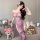 Woman modeling sheer purple one-shoulder qipao lingerie with floral hair accessory, seated on sofa with teddy bears and roses...