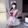 A person wearing a white maid costume with a red bow, fluffy cat ears, and ruffled details sits next to an open laptop. the o...