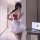 A person wearing a white maid costume with a red bow, fluffy cat ears, and thigh-high stockings poses indoors next to an open...