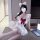 A person wearing a white cosplay maid costume with a red bow, fluffy ears, and ruffled details sits beside an open laptop.