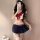 A woman poses in a playful sailor-themed outfit, featuring a white crop top with a red bow and navy pleated skirt, perfect fo...
