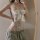 Woman wearing white lace bodysuit with bow, sheer panels and cut-outs, paired with gray sweatpants.
