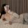 Woman lounging in white pure temptation lace bodysuit, sheer romantic lingerie with off-shoulder sleeves and matching shorts.