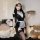 A woman poses wearing a black maid costume with white accents, holding a tray. the outfit features lace details and thigh-hig...