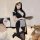 A woman poses wearing a black maid costume with lace details, holding a tray. the outfit features a revealing design and thig...