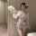A woman poses with a feather fan, wearing a delicate pink floral kimono-style sleepwear set. the outfit features a tie belt a...