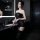 Woman wearing black sheer bodysuit with lace details in modern bathroom setting. pure & tempting lingerie bodysuit - sheer se...