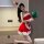 A woman poses wearing a festive christmas-themed sleepwear outfit, featuring a red dress with white lace trimmings and a sant...