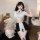 Woman modeling white and black nun-themed cosplay lingerie set with sheer cut-out bust, bodycon mini skirt, and cross details...