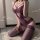 Woman wearing purple lace bodysuit with sheer mesh and elegant cutouts, paired with matching thigh-high stockings.