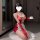 A woman poses in a red sheer mesh costume with lace details, holding a cup. the outfit features a ripped design and long glov...