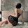 A woman sits on a rug beside a bathtub wearing a black lace sheer sleep dress with a step-mom style backless design, featurin...
