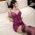 A woman lounges on a bed wearing a purple lace chemise with a decorative emblem, paired with matching lace stockings, creatin...