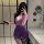 A woman poses in a bathroom wearing a purple ol secretary sexy lingerie set featuring a deep v lace sheer tight fit skirt out...