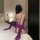 Woman wearing purple plus size lace bodysuit with long gloves, seated on bed in bedroom setting.