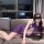 Woman wearing purple sheer lace lingerie set with open-crotch mesh bodysuit and high slit, lounging on sofa.