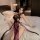 A woman lounges on a bed wearing a purple high-slit cheongsam lingerie set, featuring sheer fabric and delicate lace details....