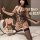 Woman modeling qingran leopard print crotchless bodysuit with rivet accents, holding a whip on bed.