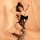 Woman wearing black lace sleepwear with butterfly design, underwire support, and push-up cups, posing on bed with sheer curta...