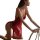 Woman wearing red qingran lace sleep dress with sheer backless design and cut-out details, kneeling beside chair.