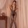Woman wearing qingyegé sheer mesh bodystocking with open-crotch design, standing by curtain and wooden side table.
