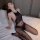 Woman wearing qingyegé sheer bodystocking with printed text, lying on bed in sensual pose.