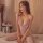 Woman wearing qingyege sheer mesh bodysuit with lace trim and matching stockings, seated on bed beside floral decor.