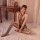 Woman wearing qingyege transparent mesh bodystocking lingerie set, sitting on bed with vintage decor background.