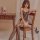 Woman wearing qingyege deep-v lace bodysuit with sheer mesh and open-crotch design, seated on wooden chair in bedroom.