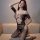 Woman modeling qingyege sheer lace bodysuit with breast cutouts and integrated fishnet stockings, posing on beige sofa.