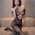 Woman wearing qingyege sexy lace bodysuit with sheer mesh, breast exposure & integrated stockings on beige sofa.