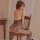 Woman wearing qingyege sheer lace bodysuit with open-crotch and off-shoulder design, seated on wooden chair.