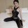 Woman wearing qingyeguo sheer black bodysuit with open-crotch tights and lace trim, posed on bed.