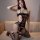 Woman wearing qingyeguo sexy transparent lace bodysuit with open-crotch design, sheer mesh nightgown on beige sofa.