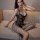 Woman wearing qingyeguo black lace bodysuit with sheer mesh and open-crotch stockings, seated on beige sofa.