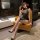 Woman in black lace cheongsam lingerie set with open-crotch design, posing elegantly on a leather chair.