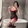 A woman poses in a bathroom wearing a black lace corset dress with red accents, paired with sheer stockings. the outfit featu...