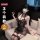 A woman wearing a black lace lingerie set with sheer fabric, sitting on a couch. the outfit features intricate designs and st...