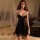 Woman in black lace lingerie set with underwire bra and matching panty, sitting on bed with sheer curtains.