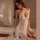 Woman in white lace lingerie set with underwire push-up bra and matching panty, sitting on bed with red roses nearby.