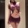 A woman models a purple lace bodycon dress featuring sheer mesh and halter neck design, creating a provocative no-remove look...