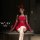Woman in red christmas lingerie set with lace gloves and bow headband, sitting on table with wine glass.