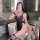 A woman poses in a bathroom wearing a black sheer maid costume with pink accents, holding a teddy bear beside her. the outfit...
